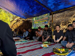 Tokoh masyarakat duduk di bawah tenda biru dalam acara launching wisata alam Tirta Sena – Curug Muntu, dengan spanduk dan makanan tradisional tersaji di atas tikar.