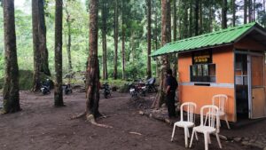 Loket tiket masuk wisata Tirta Sena - Curug Muntu di tengah hutan pinus dengan suasana alami dan motor pengunjung terparkir di area pepohonan